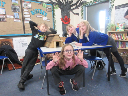 Four schoolchildren gather round a table in a classroom, showing off their wooden hedgehog house